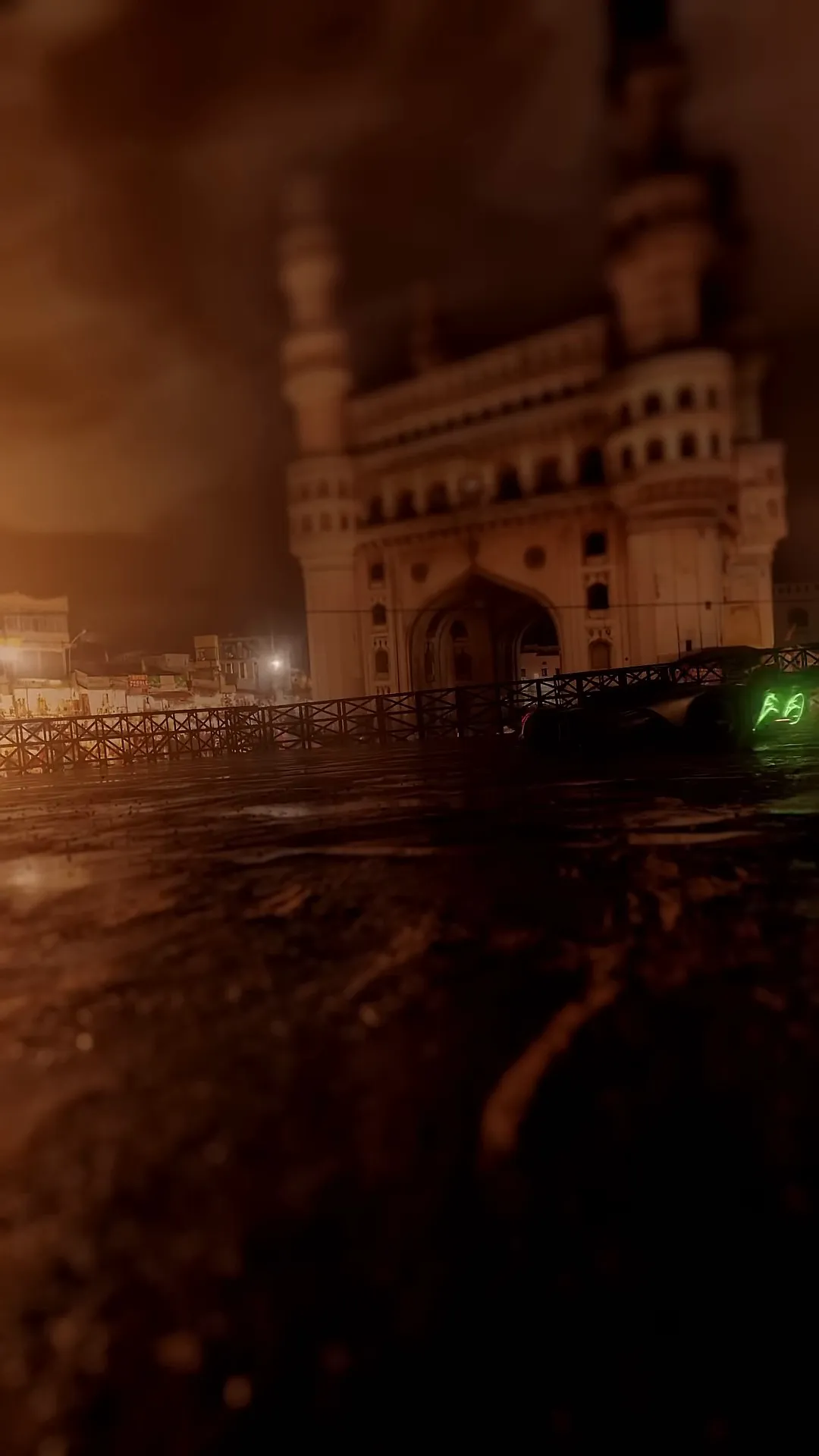 A white sports car with red lights drifts on a wet plaza at night in front of the Charminar, its minarets glowing warm through smoke.